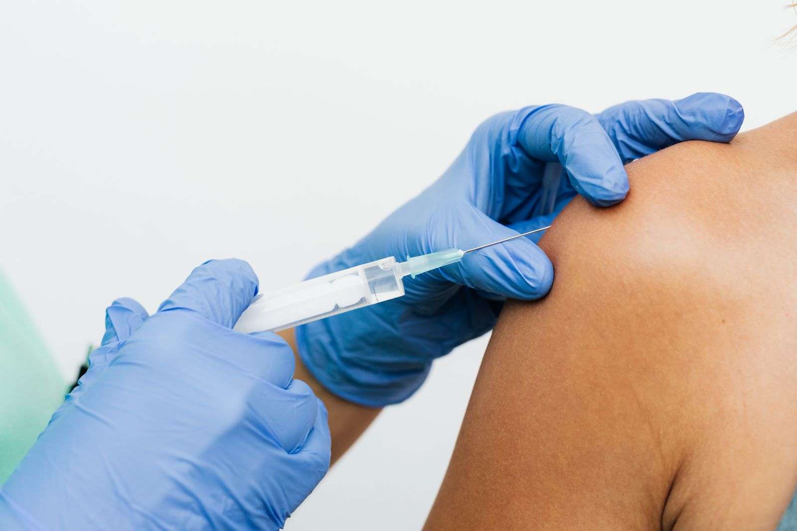 Mãos com luvas aplicando uma injeção no braço