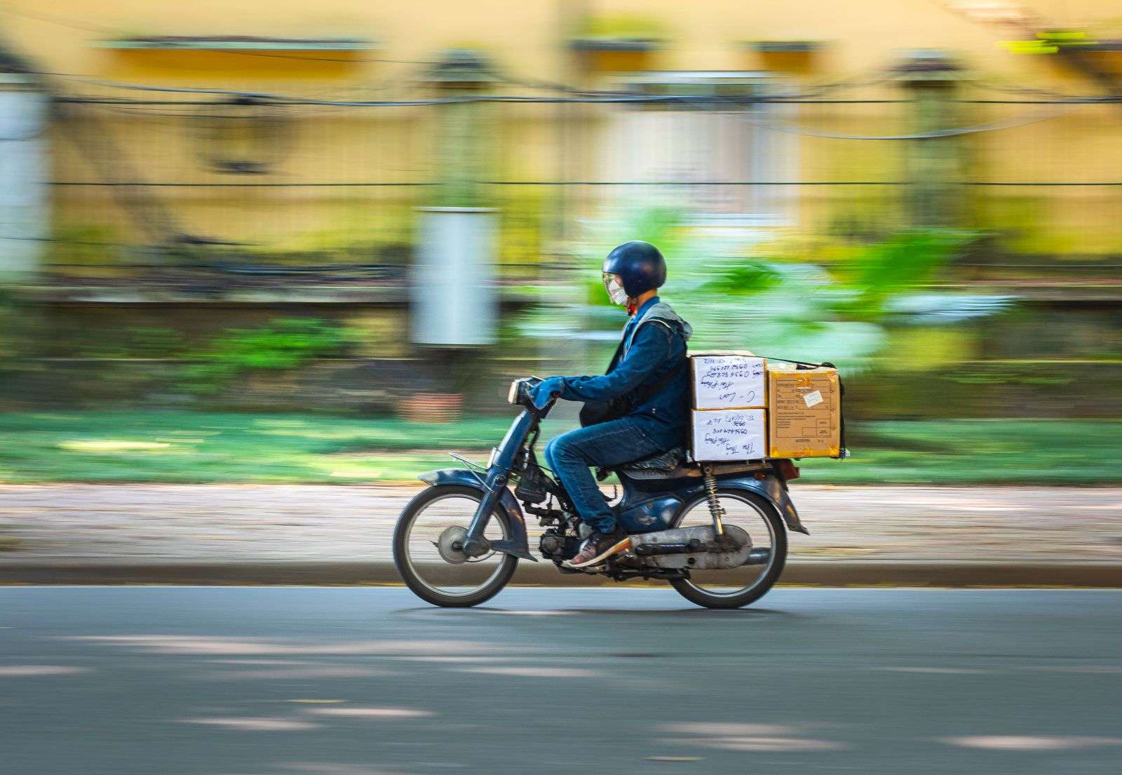 Entregador de moto levando caixas de encomenda pela rua