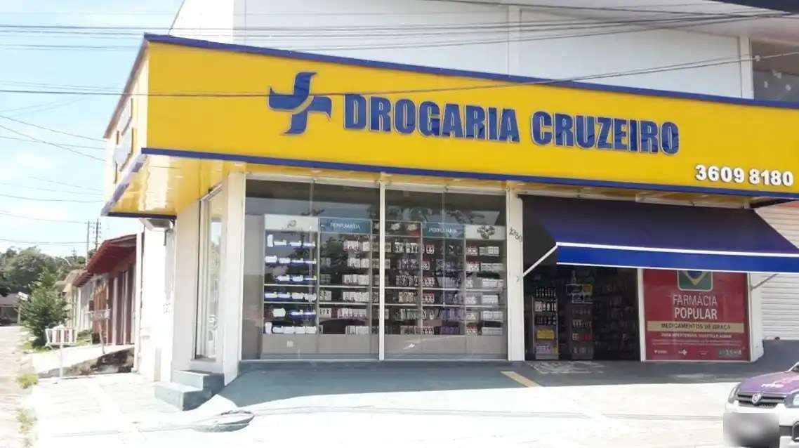 Fachada amarela da Drogaria Cruzeiro na Av. Liberdade, com o letreiro azul e a faixa do Farmácia Popular